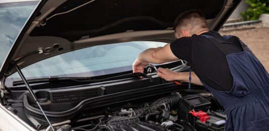 Jak kupić używane auto po flotowe i nie żałować – praktyczny poradnik dla kierowców Mechanik naprawia silnik samochodu na zewnątrz w słoneczny dzień