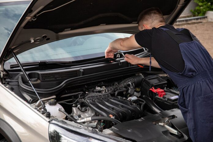 Mechanik naprawia silnik samochodu na zewnątrz w słoneczny dzień Mechanik naprawia silnik samochodu na zewnątrz w słoneczny dzień