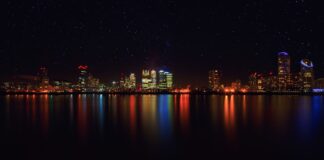 Nocna panorama miasta z odbiciami świateł w wodzie i gwiaździstym niebem