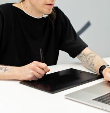 Tatuażysta pracuje przy tablecie graficznym i laptopie w pracowni