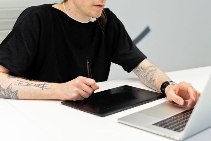 Tatuażysta pracuje przy tablecie graficznym i laptopie w pracowni