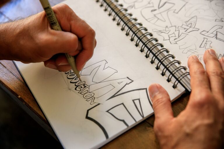 Dłonie szkicujące projekt graffiti w spiralnym notesie na stole