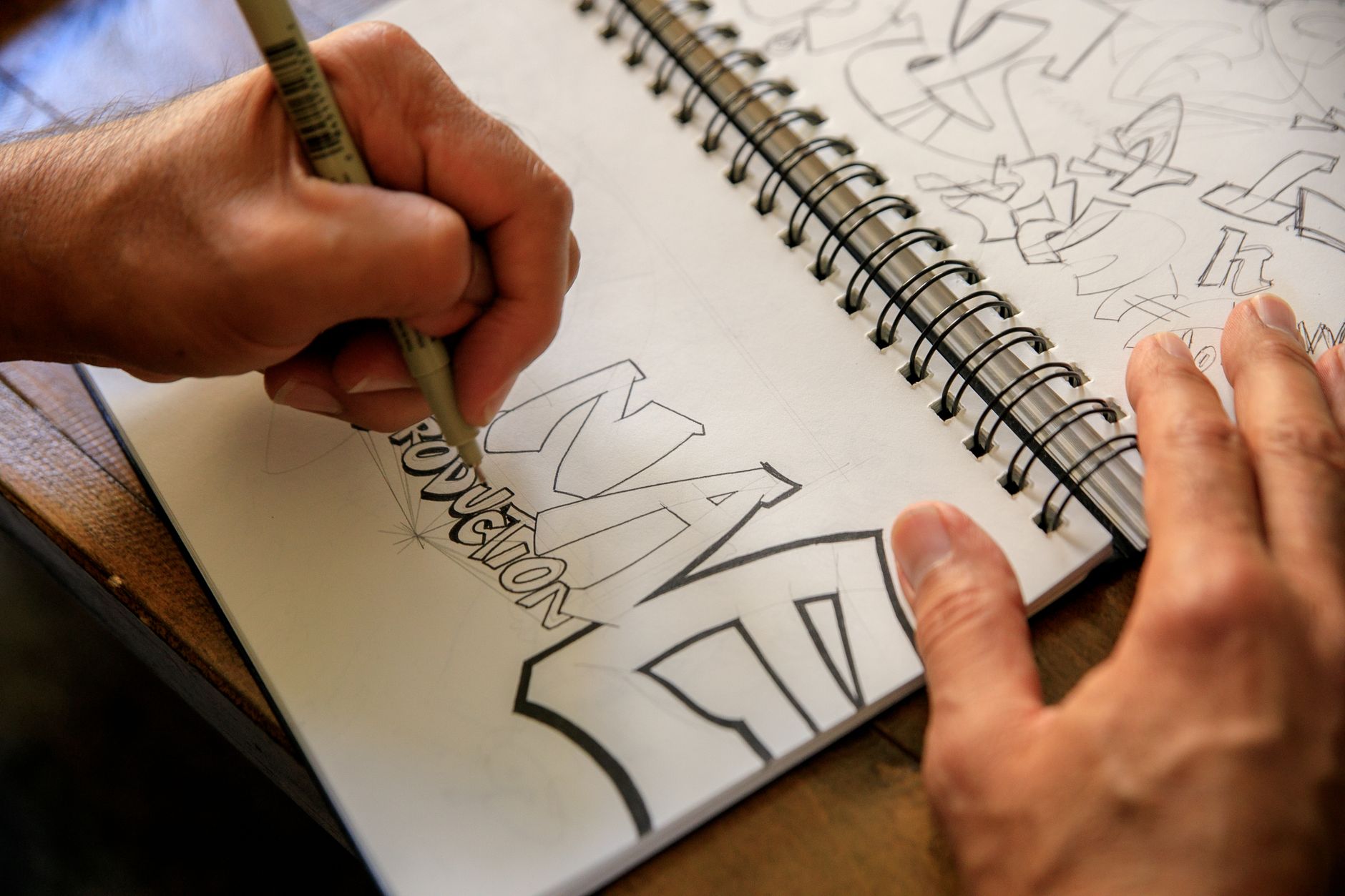 Dłonie szkicujące projekt graffiti w spiralnym notesie na stole
