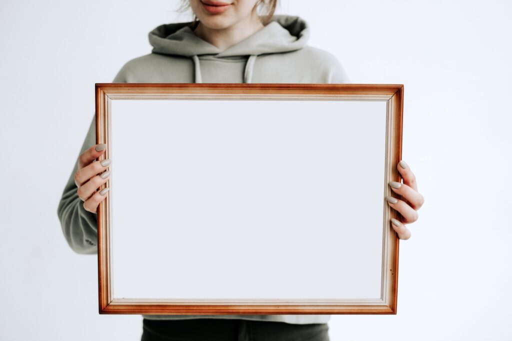 Osoba w bluzie z kapturem trzyma pustą drewnianą ramę do mockupu